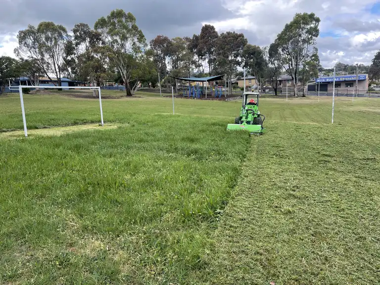 Avant loader with flail mower slashing long grass at a local sports field or park