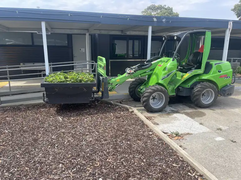 Avant loader safely lifting and moving a large planter box at a commercial site