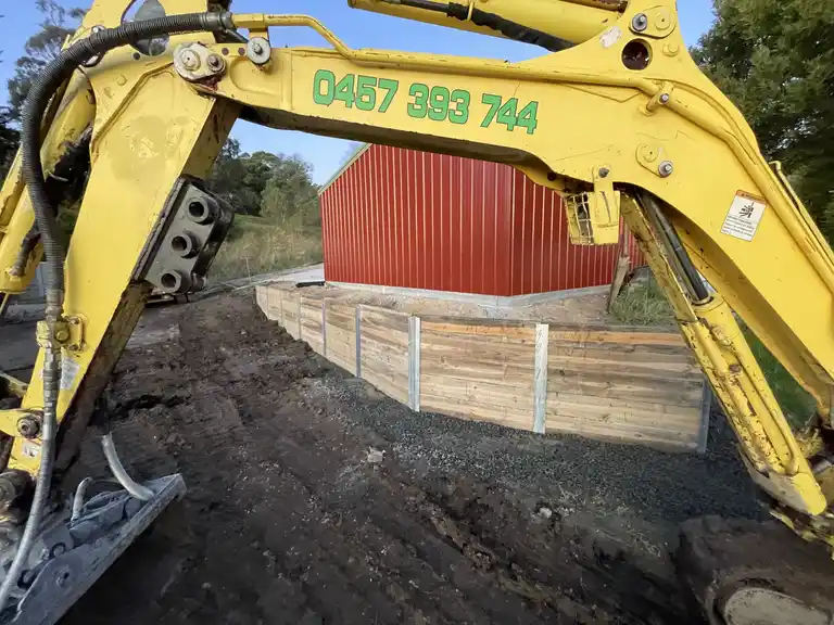 Yellow mini excavator building a timber retaining wall in Gippsland