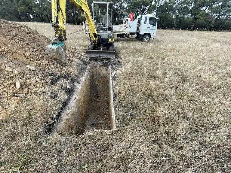 Mini excavator digging a deep trench for drainage in a Gippsland paddock