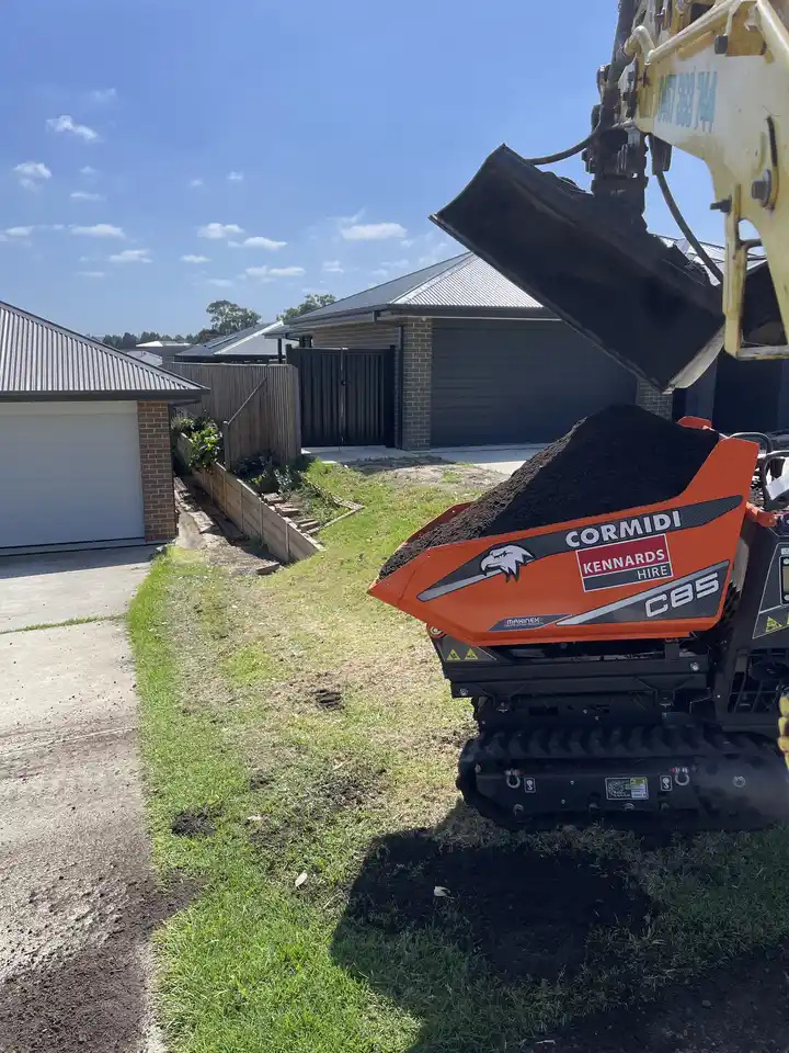 Excavator loading soil into a tracked mini dumper for efficient site clearing