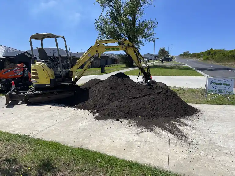 Mini excavator moving a large pile of soil on a residential driveway in Latrobe Valley