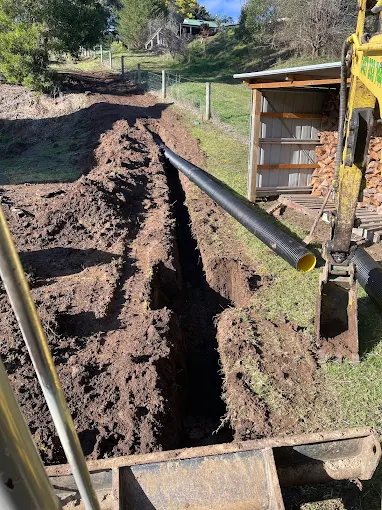 Excavator digging a trench for agricultural drainage pipe installation