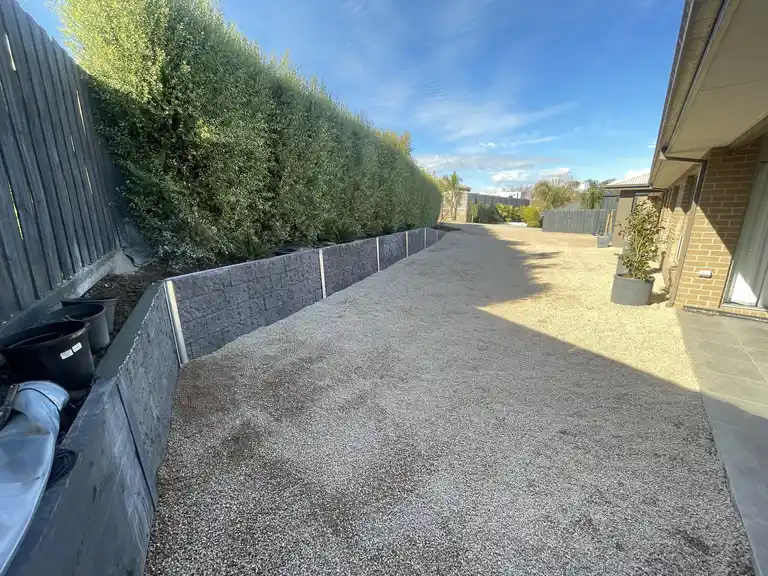 Long block retaining wall installation alongside a crushed rock driveway