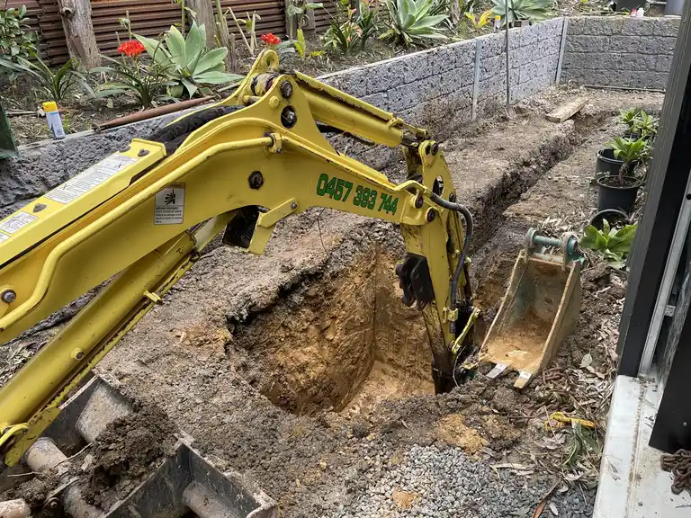 Mini excavator bucket trenching safely next to an existing block retaining wall